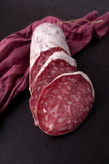 Delicacy raw-dried sausage, red cloth on a black background. Close-up.