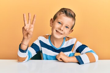 Adorable caucasian kid wearing casual clothes sitting on the table showing and pointing up with...