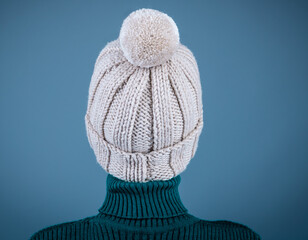 View from the back of a girl in a wool hat with a pompom. Grey background.