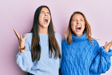 Hispanic family of mother and daughter wearing wool winter sweater crazy and mad shouting and...