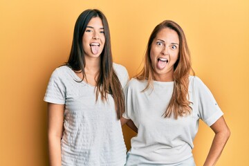 Hispanic family of mother and daughter wearing casual white tshirt sticking tongue out happy with funny expression. emotion concept.