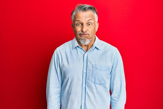 Middle age grey-haired man wearing casual clothes puffing cheeks with funny face. mouth inflated with air, crazy expression.