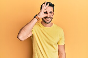 Young hispanic man wearing casual clothes and glasses doing ok gesture with hand smiling, eye looking through fingers with happy face.