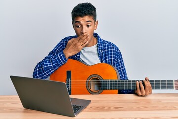 Young handsome african american man learning classical guitar from online tutorial covering mouth...