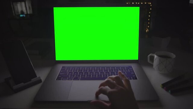 Female hands typing on a track pad. Laptop with green screen. Dark office. Locked. Perfect to put your own image or video. Track with perspective corner pin.  