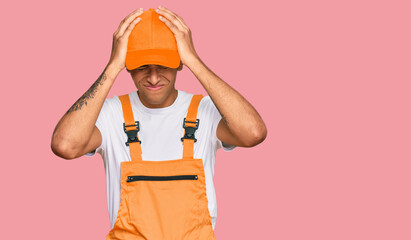 Young handsome african american man wearing handyman uniform suffering from headache desperate and stressed because pain and migraine. hands on head.