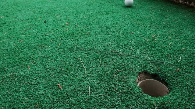 Making mistakes in life, missing goals, far from winning, another failure on the road to success. Mini golf on green lawn outside, missed shot, trying again and learning by challenging yourself.