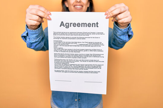 Woman holding agreement document paper standing over isolated yellow background