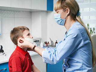 Female ENT doctor taking off or putting on a protective face mask from a boy patent before medical examination