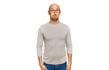 Bald man with beard wearing casual clothes and glasses puffing cheeks with funny face. mouth...