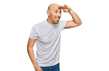 Bald man with beard wearing casual white t shirt very happy and smiling looking far away with hand over head. searching concept.