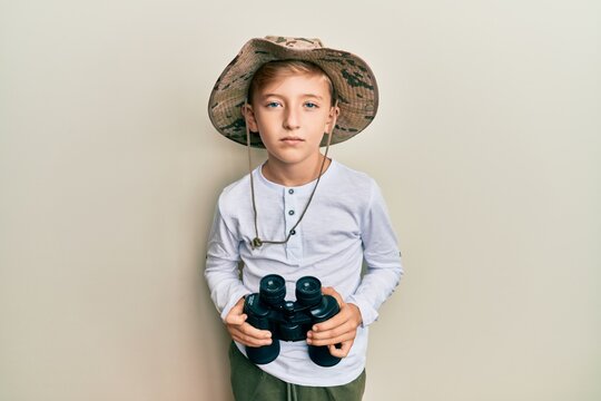 Little caucasian boy kid wearing explorer hat holding binoculars relaxed with serious expression on face. simple and natural looking at the camera.