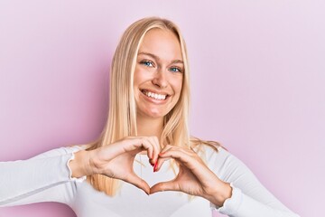 Young blonde girl wearing casual clothes smiling in love doing heart symbol shape with hands. romantic concept.