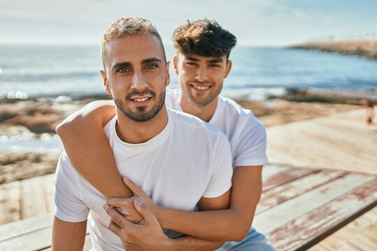 Young gay couple smiling happy sitting on the bench at the beach promenade.