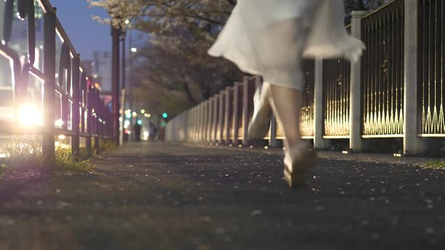 Young woman run at empty alley along sidewalk, low camera selective focused shot. Tourist girl explore Tokyo city during hanami season. Evening time at Sotobori alley. Cherry flowers petals on ground