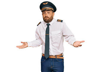 Handsome man with beard wearing airplane pilot uniform clueless and confused expression with arms...