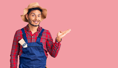 Handsome latin american young man weaing handyman uniform smiling cheerful presenting and pointing with palm of hand looking at the camera.