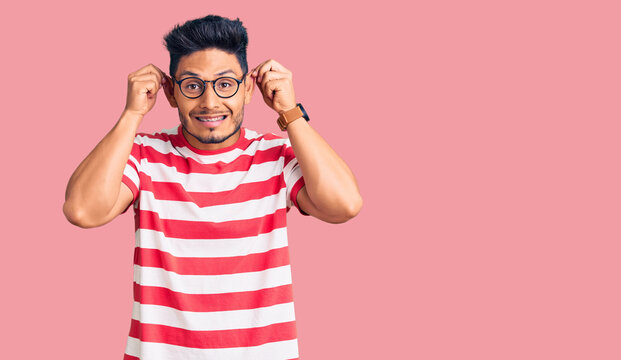 Handsome latin american young man wearing casual clothes and glasses smiling pulling ears with fingers, funny gesture. audition problem