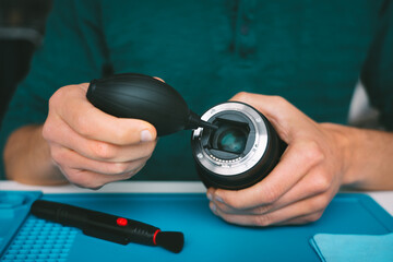 Photographer cleaning camera lens with dust cleaner, air blower or vacuum pump. Photography equipment care