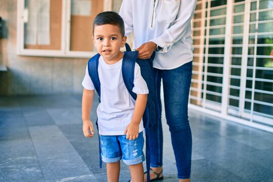 Adorable latin student boy and mom at school. Mother preparing kid putting up backpack.