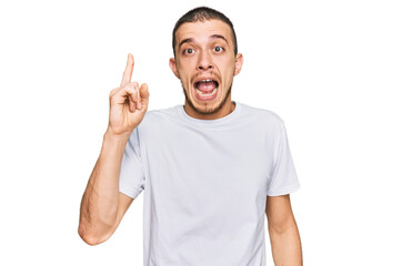 Fototapeta premium Hispanic young man wearing casual white t shirt pointing finger up with successful idea. exited and happy. number one.