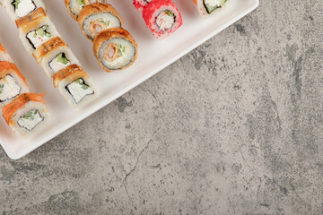 A white board with different types of delicious sushi rolls on stone table