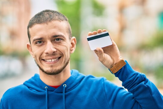 Young hispanic man smiling happy holding credit card at the city