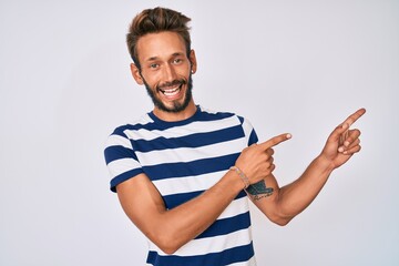 Handsome caucasian man with beard wearing casual striped t-shirt smiling and looking at the camera pointing with two hands and fingers to the side.