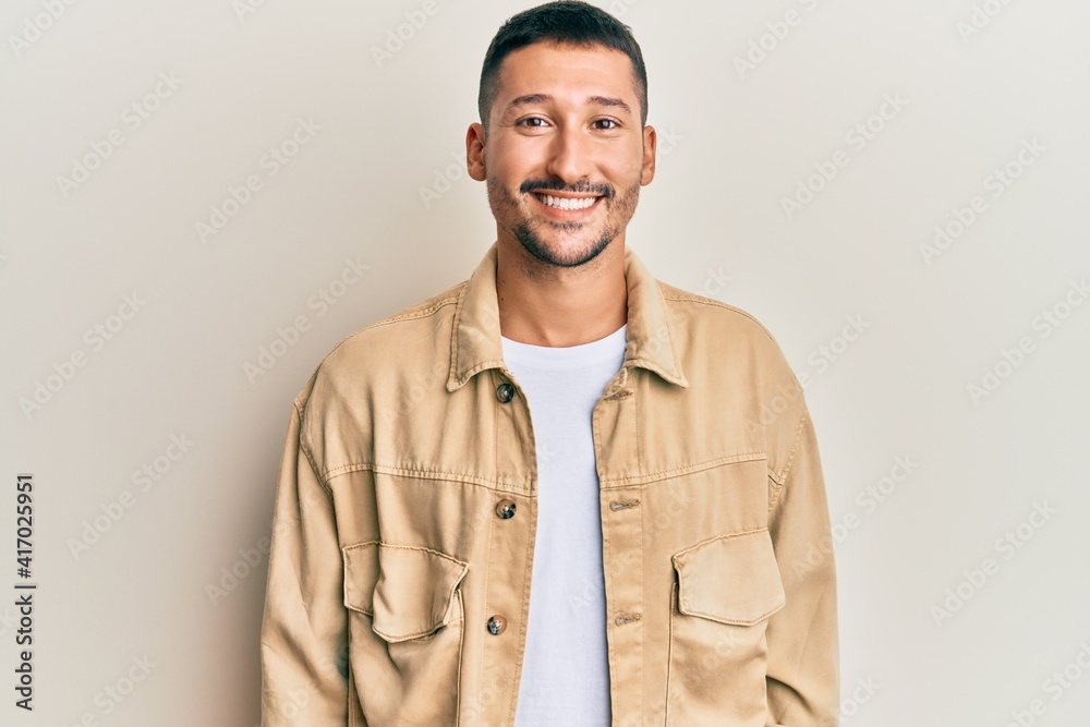 Poster handsome man with tattoos wearing casual brown denim jacket with a happy and cool smile on face. luc