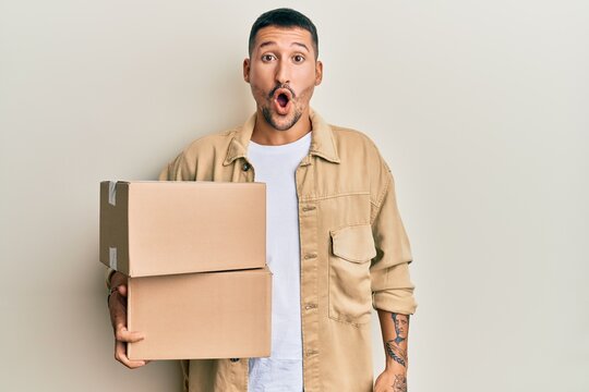 Handsome man with tattoos holding delivery package scared and amazed with open mouth for surprise, disbelief face