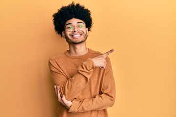 Fototapeta na wymiar Young african american man with afro hair wearing casual winter sweater with a big smile on face, pointing with hand and finger to the side looking at the camera.
