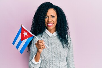 Middle age african american woman holding cuba flag looking positive and happy standing and smiling with a confident smile showing teeth