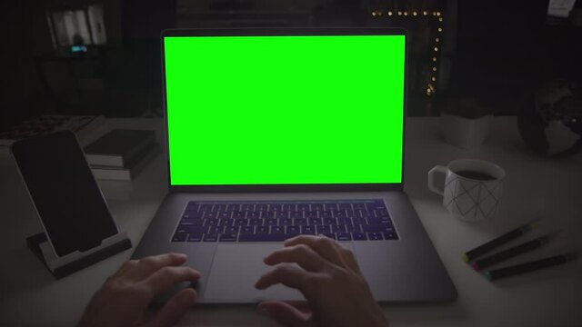 Laptop with green screen. Female hands typing on a track pad. Dark office. Perfect to put your own image or video. Track with perspective corner pin.  
