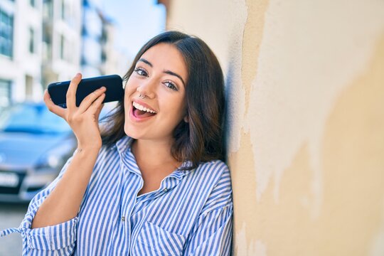 Young hispanic businesswoman smiling happy listening audio message using smartphone at the city.