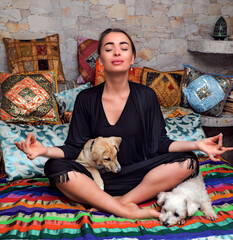 The girl sits in a lotus pose on the bed, next to lie two dogs.
