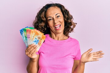 Middle age hispanic woman holding swiss franc banknotes celebrating achievement with happy smile and winner expression with raised hand