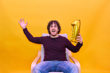 Young adult holding balloon of number one. Celebrating victory playing videogames. Casual clothing. Over isolated yellow background.