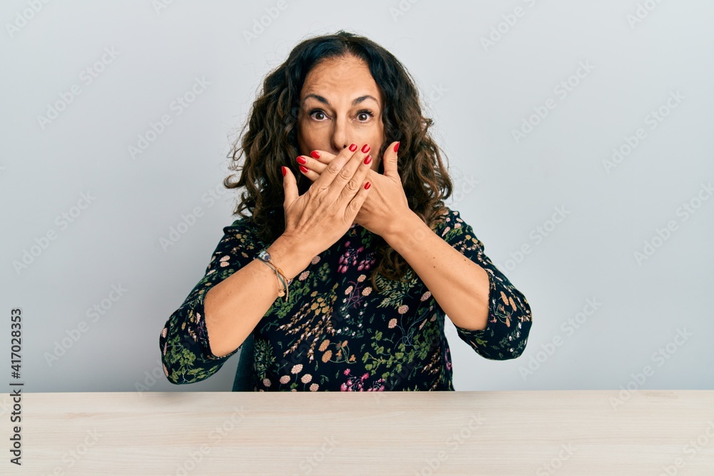 Sticker Beautiful middle age woman wearing casual clothes sitting on the table shocked covering mouth with hands for mistake. secret concept.