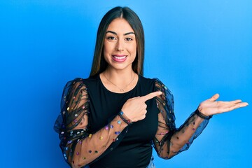 Young hispanic woman wearing casual clothes amazed and smiling to the camera while presenting with hand and pointing with finger.