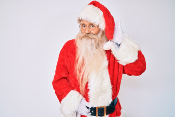 Old senior man with grey hair and long beard wearing santa claus costume with suspenders smiling with hand over ear listening an hearing to rumor or gossip. deafness concept.