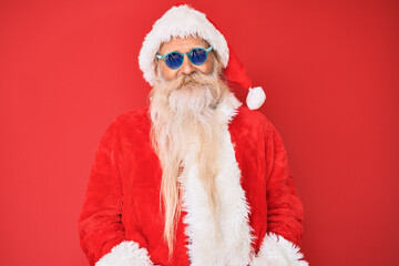 Old senior man wearing santa claus costume and sunglasses looking positive and happy standing and smiling with a confident smile showing teeth