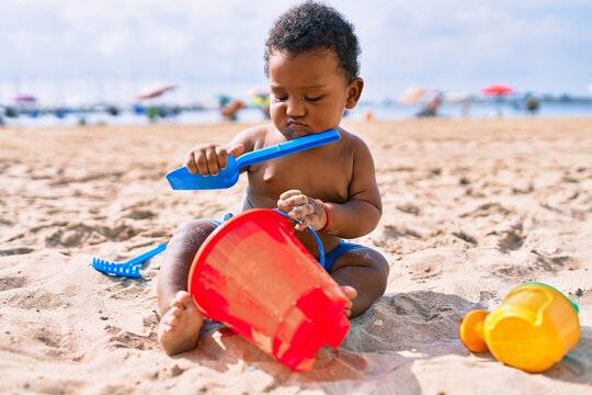Adorable african american toddler playing with toys sitting on the sand at the beach.