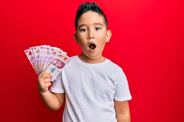 Little boy hispanic kid holding 50 mexican pesos banknotes scared and amazed with open mouth for...