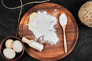 Flour and eggs on wooden board with spoons on black background