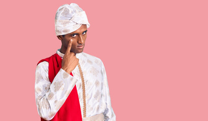 African handsome man wearing tradition sherwani saree clothes pointing to the eye watching you gesture, suspicious expression