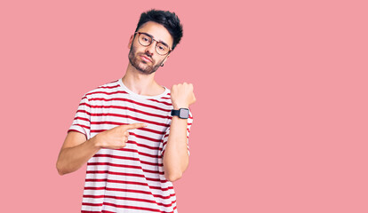 Young hispanic man wearing casual clothes in hurry pointing to watch time, impatience, looking at...