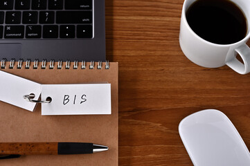On the desk there is a laptop, a cup of coffee, and a word book with the word BIS written on it. It was an abbreviation for the financial term Bank for International Settlements.