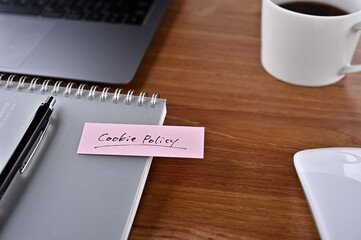 On the desk there is a laptop, a cup of coffee, and a sticky note with the word financial term Cookie Policy.