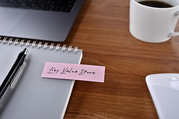 On the desk there is a laptop, a cup of coffee, and a sticky note with the word financial term key value store.