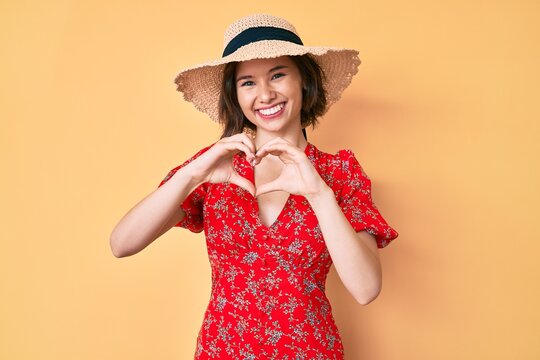 Young beautiful girl wearing summer hat smiling in love showing heart symbol and shape with hands. romantic concept.